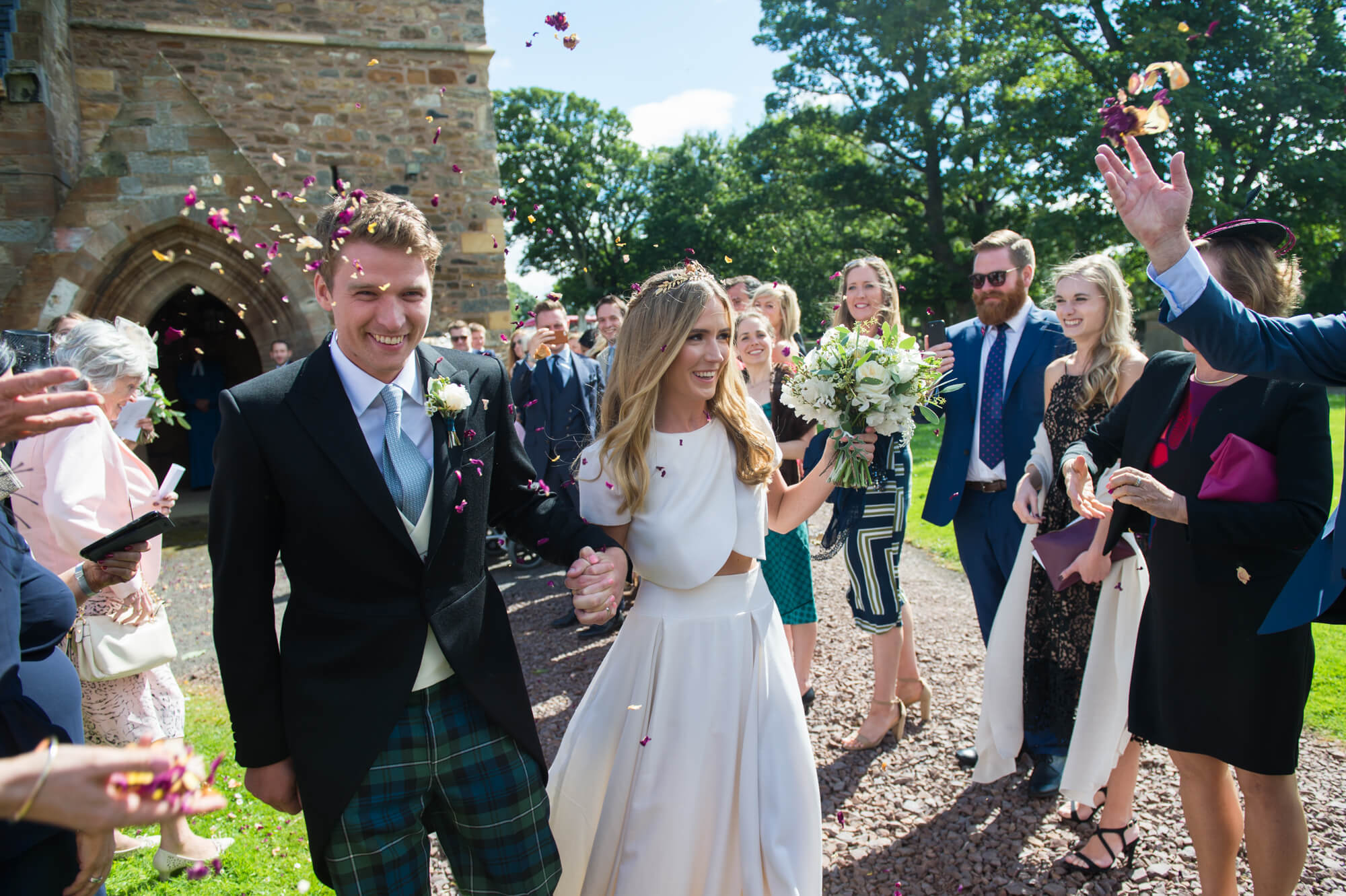 bride and groom leaving aberlady church through a confetti line with sunshine and blue sky